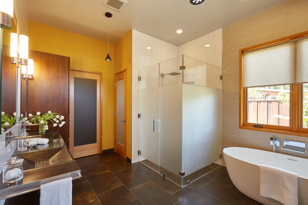 This is an example of a mid-sized modern master bathroom in San Francisco with an integrated sink, recessed-panel cabinets, medium wood cabinets, a freestanding tub, a curbless shower, a wall-mount toilet, gray tile, ceramic tile, ceramic floors, beige walls, stainless steel benchtops, multi-coloured floor and a hinged shower door.