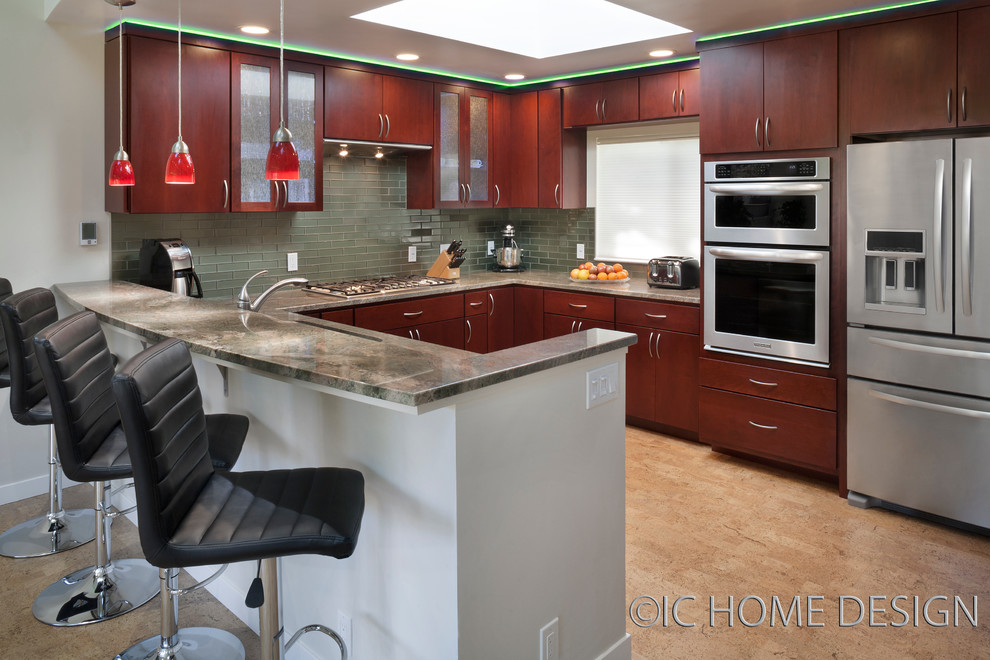 This is an example of a modern u-shaped open plan kitchen in San Francisco with flat-panel cabinets, dark wood cabinets, granite benchtops, green splashback, glass tile splashback, stainless steel appliances, cork floors and a peninsula.
