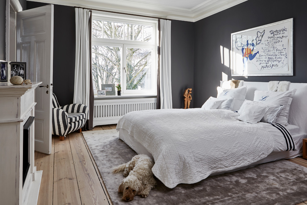 Large contemporary master bedroom in Hamburg with black walls, a standard fireplace, a wood fireplace surround, brown floor and medium hardwood floors.