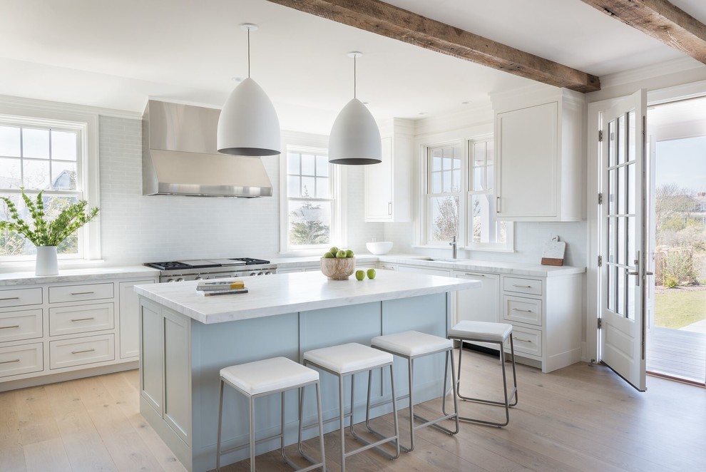 Design ideas for a mid-sized beach style l-shaped kitchen in Providence with an undermount sink, white cabinets, marble benchtops, white splashback, glass tile splashback, stainless steel appliances, light hardwood floors, with island, beige floor and shaker cabinets.