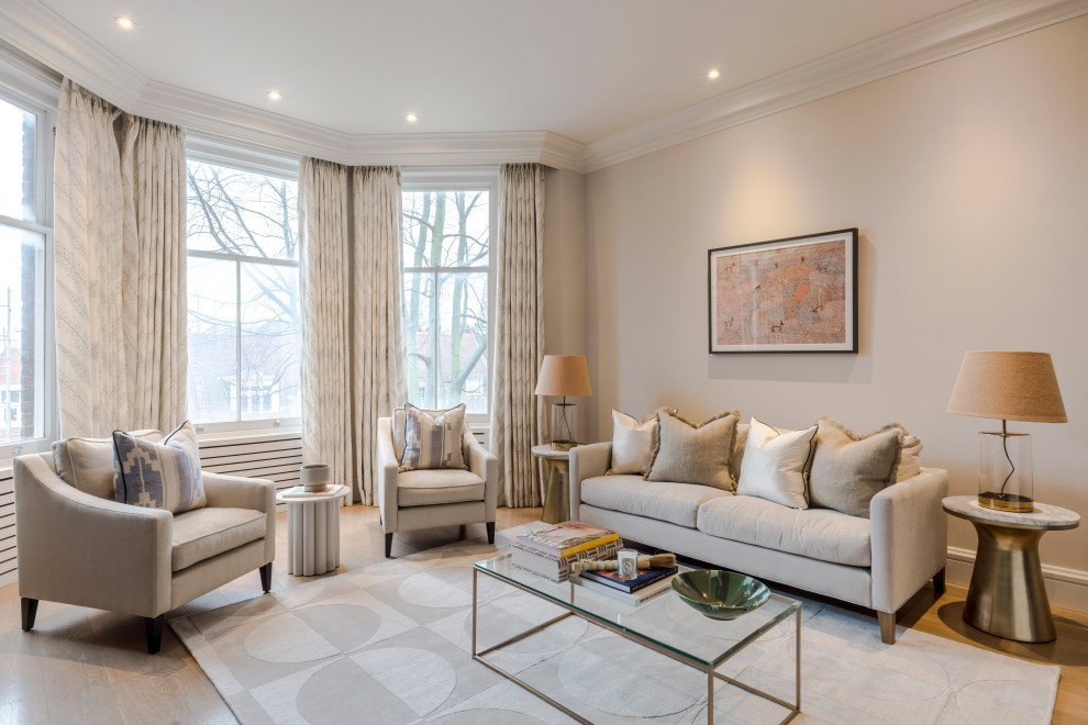This is an example of a transitional living room in London with beige walls, light hardwood floors and beige floor.