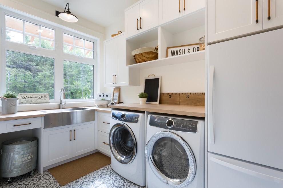 Design ideas for a beach style l-shaped utility room in Other with a farmhouse sink, shaker cabinets, white cabinets, wood benchtops, white walls, a side-by-side washer and dryer, grey floor and beige benchtop.