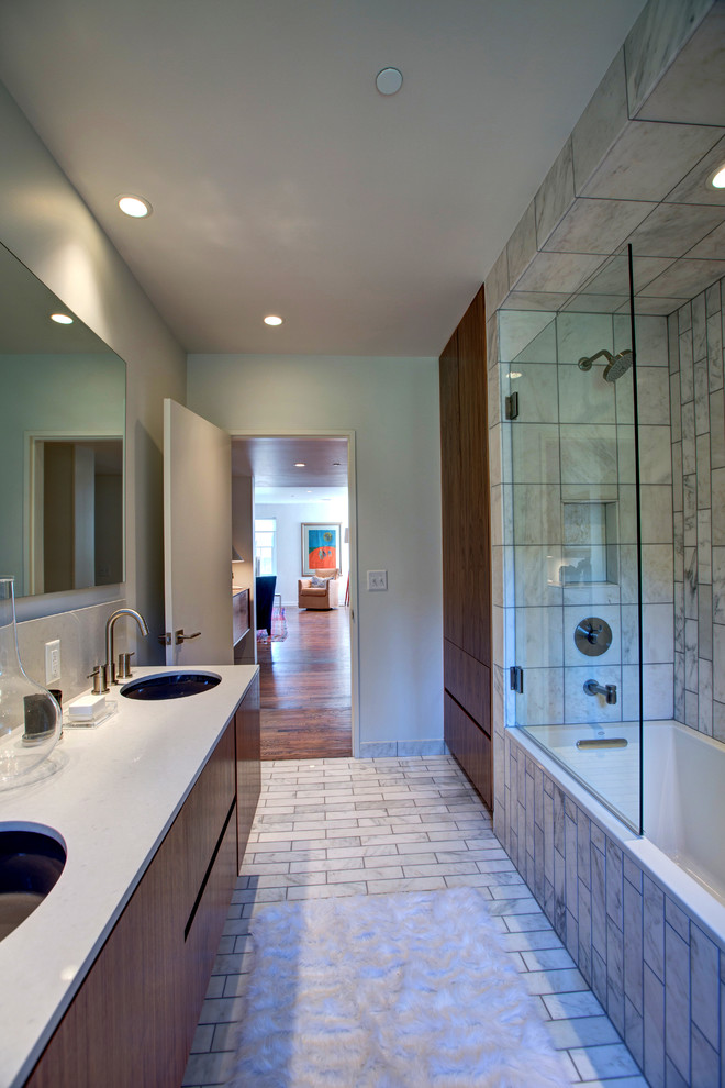 This is an example of a mid-sized contemporary 3/4 bathroom in Oklahoma City with an undermount sink, flat-panel cabinets, medium wood cabinets, engineered quartz benchtops, a drop-in tub, a shower/bathtub combo, a wall-mount toilet, white tile, stone tile, white walls and marble floors.