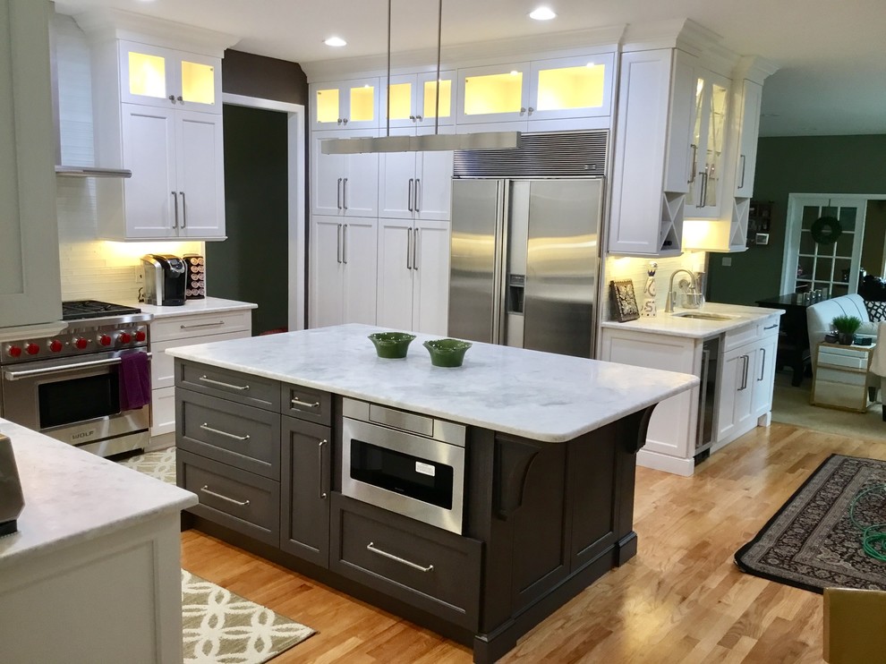 Inspiration for a large transitional u-shaped light wood floor and beige floor open concept kitchen remodel in New York with beaded inset cabinets, white cabinets, marble countertops, an island, white backsplash, an undermount sink and stainless steel appliances