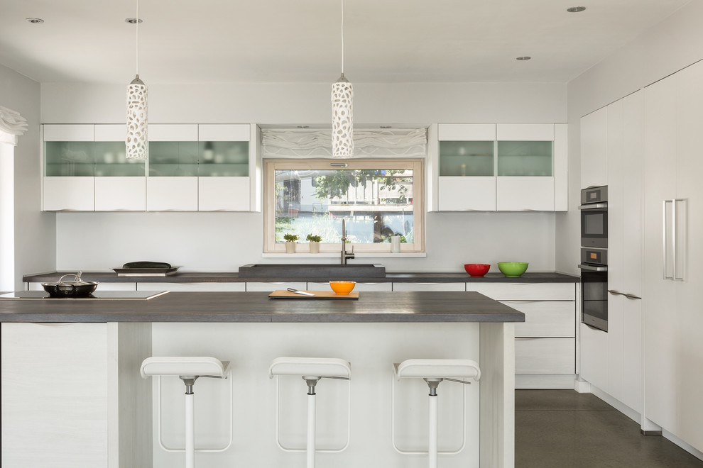Inspiration for a mid-sized contemporary kitchen in Boston with flat-panel cabinets, white cabinets, concrete floors, with island, a drop-in sink and panelled appliances.