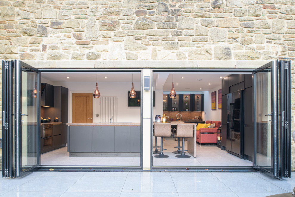 Moderne Wohnküche mit schwarzen Schränken, Küchenrückwand in Braun, schwarzen Elektrogeräten und brauner Arbeitsplatte in Sonstige