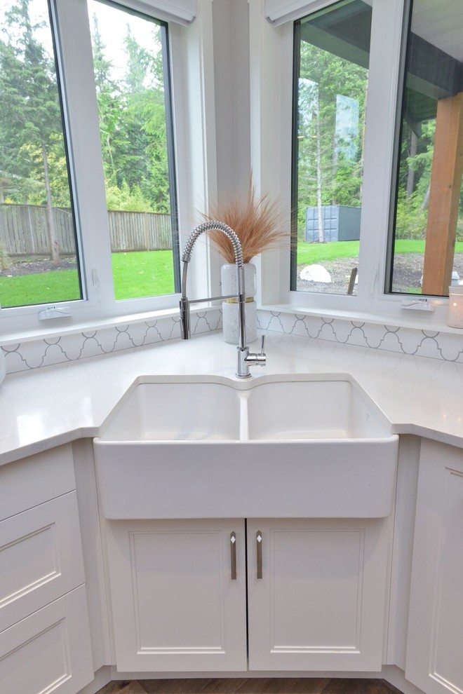 Example of a minimalist home design design in Vancouver with a farmhouse sink, raised-panel cabinets, white cabinets, quartzite countertops, white backsplash, mosaic tile backsplash, stainless steel appliances and an island
