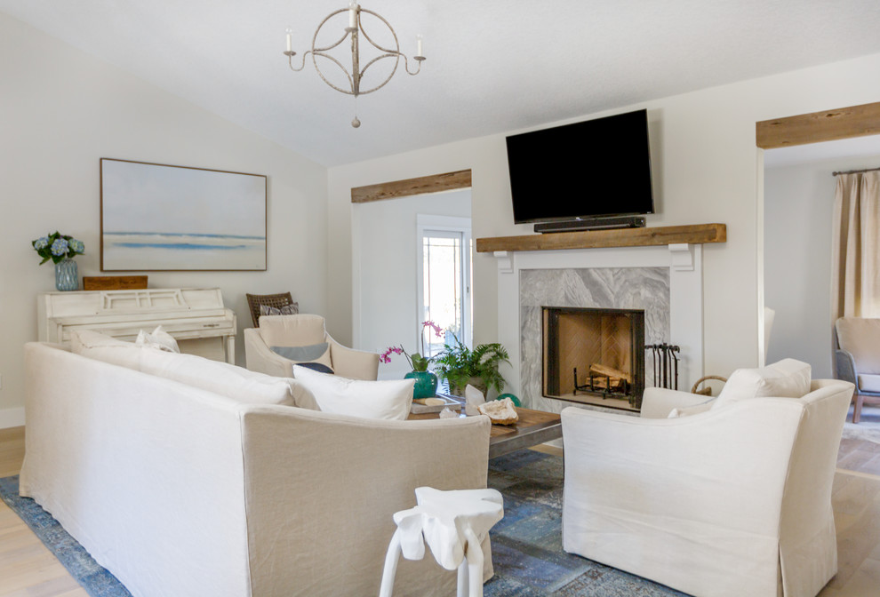 This is an example of a mid-sized beach style formal open concept living room in Jacksonville with beige walls, light hardwood floors, a standard fireplace, a stone fireplace surround, a wall-mounted tv and beige floor.