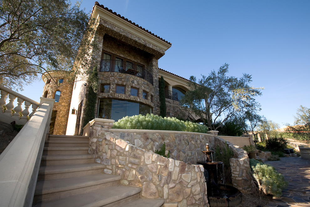 This is an example of an expansive mediterranean three-storey beige house exterior in San Diego with stone veneer, a hip roof and a tile roof.