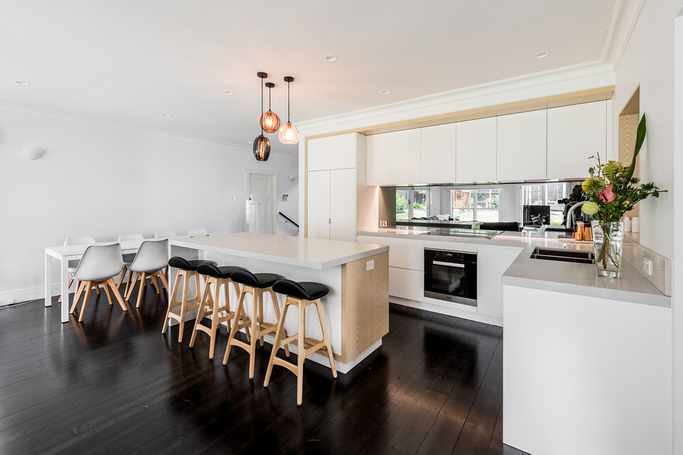 Inspiration for a large contemporary l-shaped open plan kitchen in Melbourne with an undermount sink, flat-panel cabinets, white cabinets, quartz benchtops, metallic splashback, mirror splashback, black appliances, dark hardwood floors, with island and brown floor.