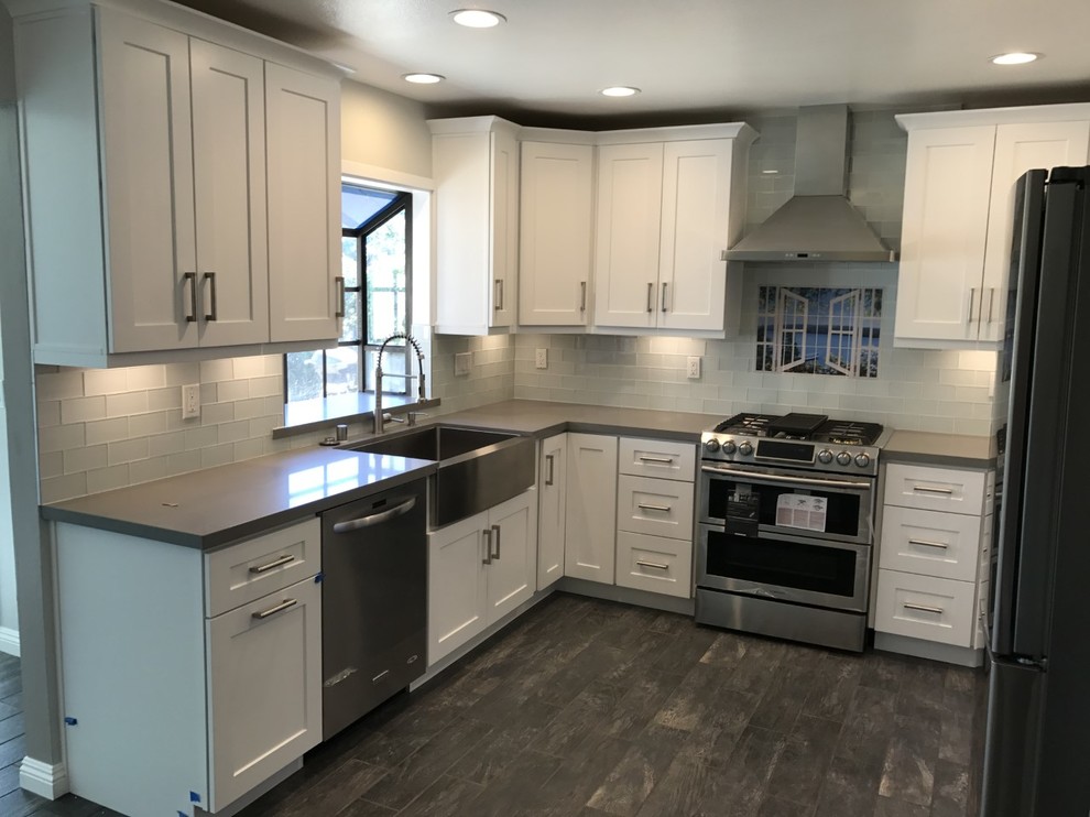 This is an example of a mid-sized contemporary u-shaped eat-in kitchen in Los Angeles with a farmhouse sink, shaker cabinets, white cabinets, quartzite benchtops, glass tile splashback, stainless steel appliances, ceramic floors, no island, brown floor, grey benchtop and grey splashback.