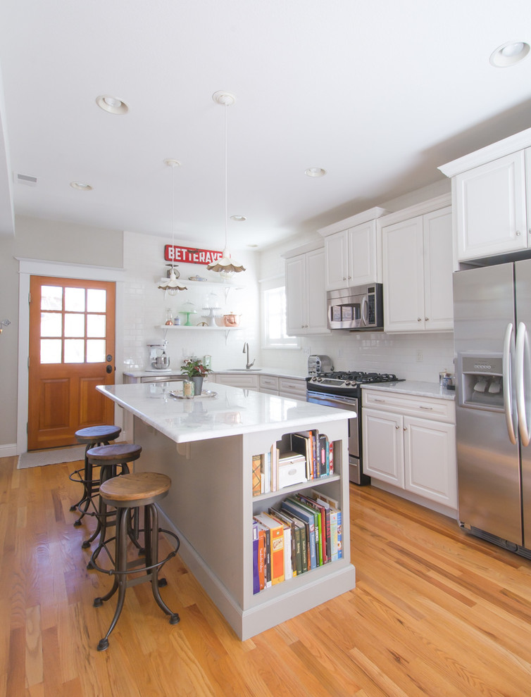 Design ideas for a mid-sized eclectic eat-in kitchen in Denver with an undermount sink, raised-panel cabinets, white cabinets, marble benchtops, white splashback, subway tile splashback, stainless steel appliances and with island.