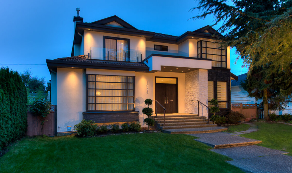 This is an example of a large modern three-storey stucco white house exterior in Vancouver with a hip roof, a tile roof and a brown roof.
