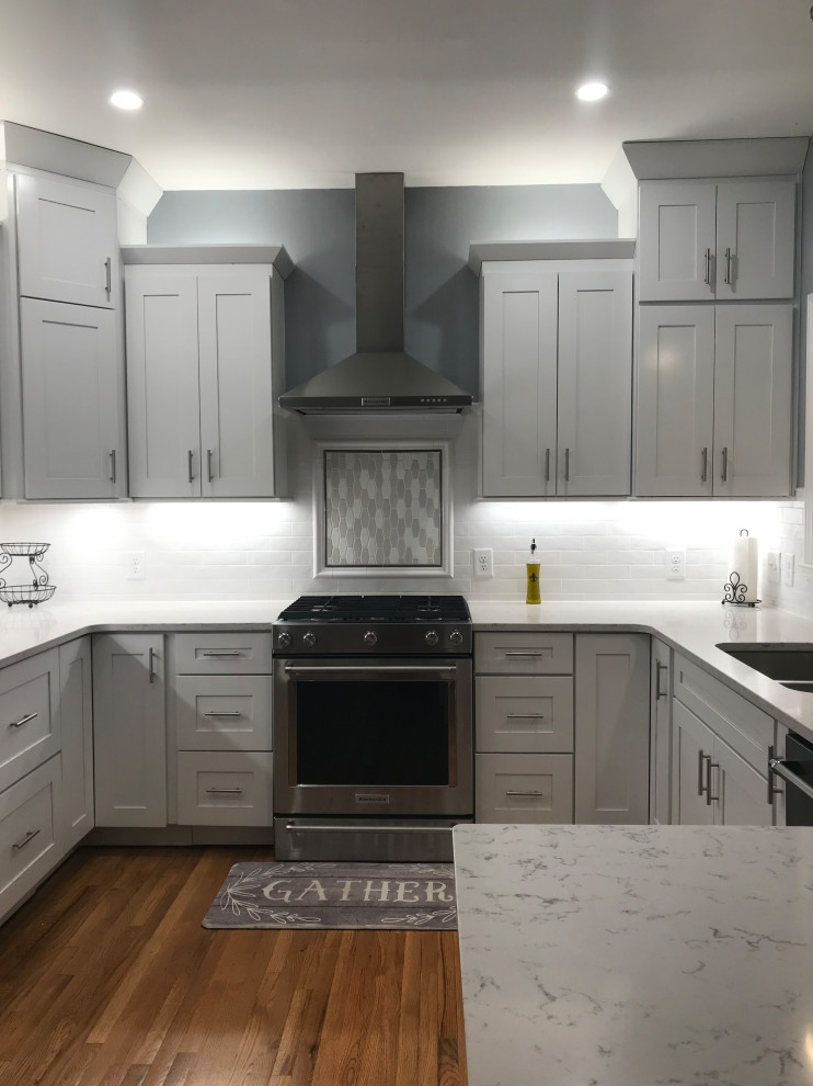 Example of a mid-sized transitional u-shaped medium tone wood floor kitchen design in Charlotte with an undermount sink, shaker cabinets, white cabinets, quartz countertops, white backsplash, subway tile backsplash, stainless steel appliances and a peninsula
