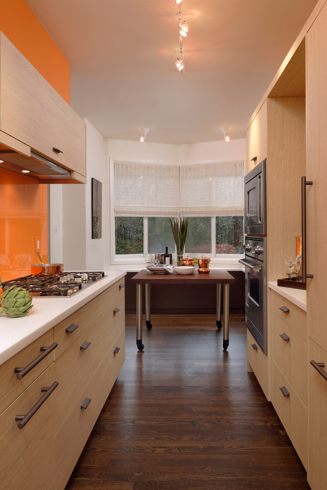 Photo of a small contemporary galley eat-in kitchen in DC Metro with an undermount sink, flat-panel cabinets, light wood cabinets, quartzite benchtops, orange splashback, stainless steel appliances, dark hardwood floors, no island and glass sheet splashback.