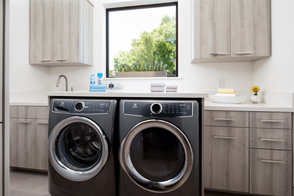 This is an example of a mid-sized contemporary single-wall dedicated laundry room in San Francisco with an undermount sink, flat-panel cabinets, grey cabinets, quartz benchtops, white walls, porcelain floors, a side-by-side washer and dryer, grey floor and white benchtop.