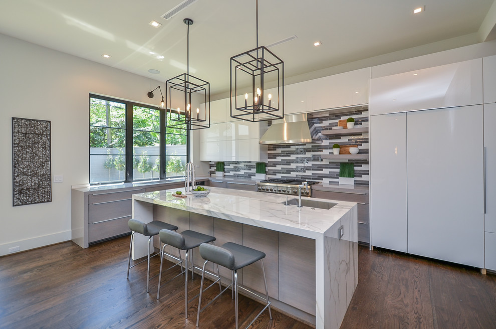 Inspiration for a mid-sized transitional l-shaped medium tone wood floor open concept kitchen remodel in Houston with a single-bowl sink, flat-panel cabinets, white cabinets, marble countertops, multicolored backsplash, glass tile backsplash, stainless steel appliances, an island and white countertops