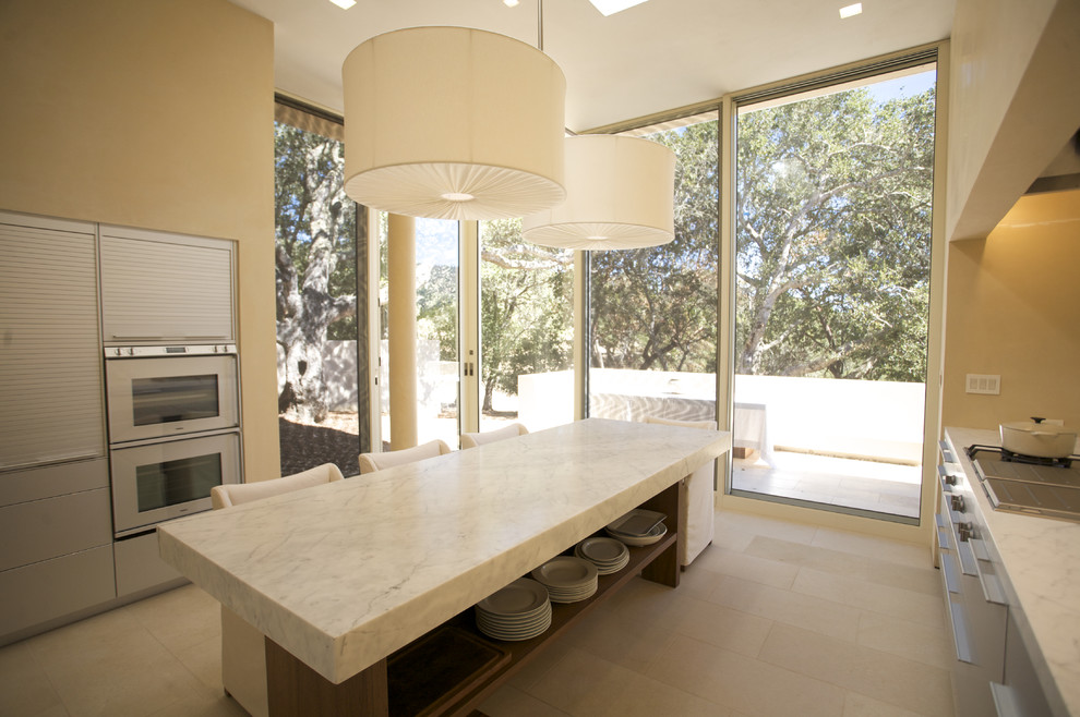 Photo of a contemporary u-shaped eat-in kitchen in San Francisco with stainless steel appliances, an undermount sink, flat-panel cabinets, stainless steel cabinets, marble benchtops, white splashback, glass tile splashback and ceramic floors.