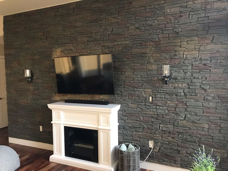 Cette image montre un salon avec une cheminée standard, un manteau de cheminée en pierre de parement et un téléviseur fixé au mur.