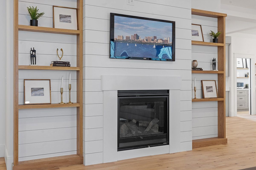 Design ideas for a large country open concept living room in Boston with white walls, light hardwood floors, a standard fireplace, a wood fireplace surround, a wall-mounted tv, beige floor, recessed and planked wall panelling.