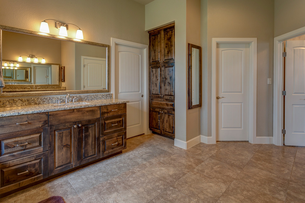 Photo of a large country master bathroom in Austin with raised-panel cabinets, dark wood cabinets, ceramic tile, ceramic floors, an undermount sink, granite benchtops, beige floor, multi-coloured benchtops, a drop-in tub, a corner shower, beige walls and a hinged shower door.