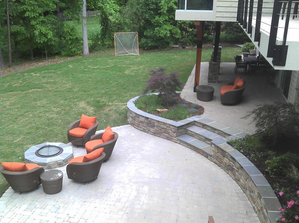 This is an example of a large arts and crafts backyard patio in Raleigh with concrete pavers, a fire feature and a roof extension.