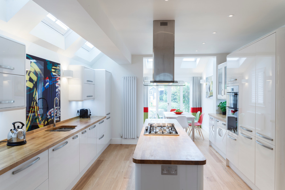Design ideas for a contemporary galley eat-in kitchen in Cambridgeshire with an undermount sink, flat-panel cabinets, white cabinets, wood benchtops, stainless steel appliances, light hardwood floors, with island and multi-coloured splashback.