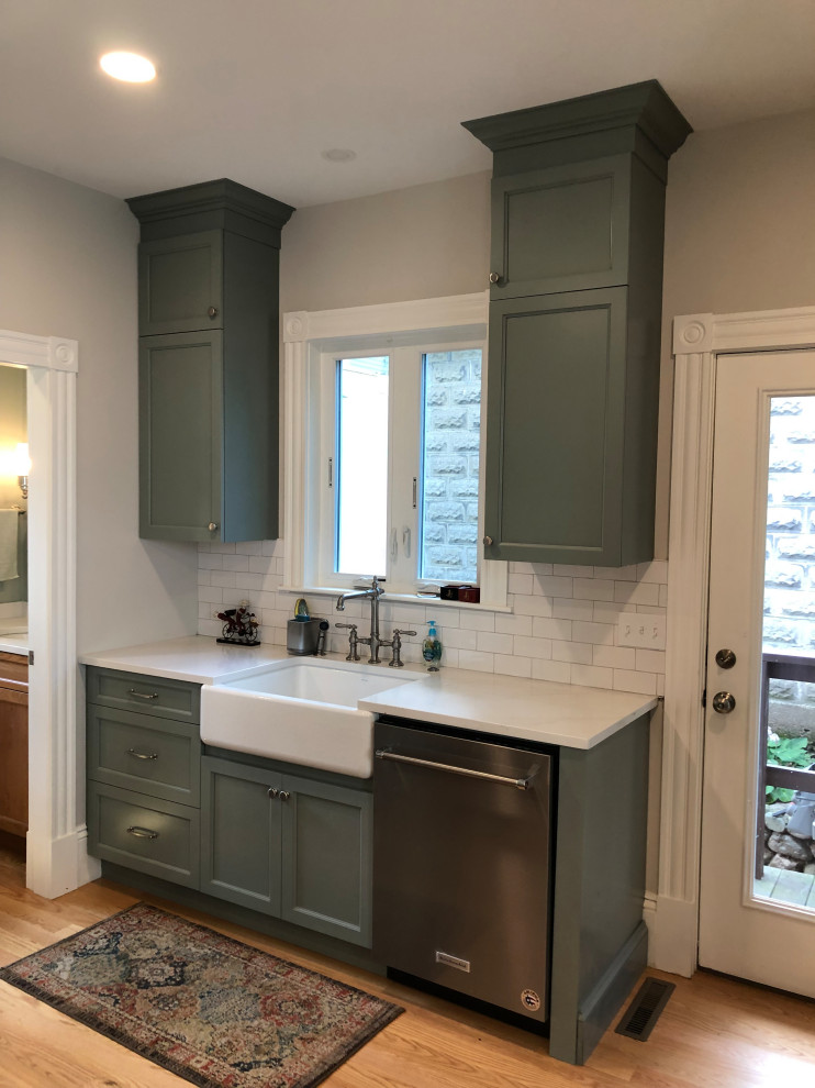This is an example of a mid-sized traditional u-shaped separate kitchen in Boston with a farmhouse sink, flat-panel cabinets, green cabinets, quartz benchtops, white splashback, ceramic splashback, stainless steel appliances, light hardwood floors, with island, brown floor and white benchtop.