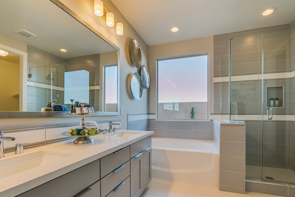 Mid-sized contemporary master bathroom in Phoenix with recessed-panel cabinets, grey cabinets, a corner tub, a corner shower, gray tile, ceramic tile, beige walls, ceramic floors, an undermount sink, solid surface benchtops, beige floor and a hinged shower door.