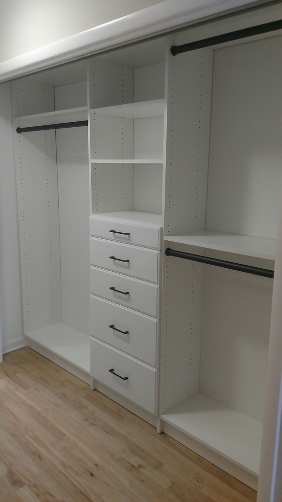 This is an example of a mid-sized modern gender-neutral built-in wardrobe in New York with flat-panel cabinets, white cabinets and light hardwood floors.