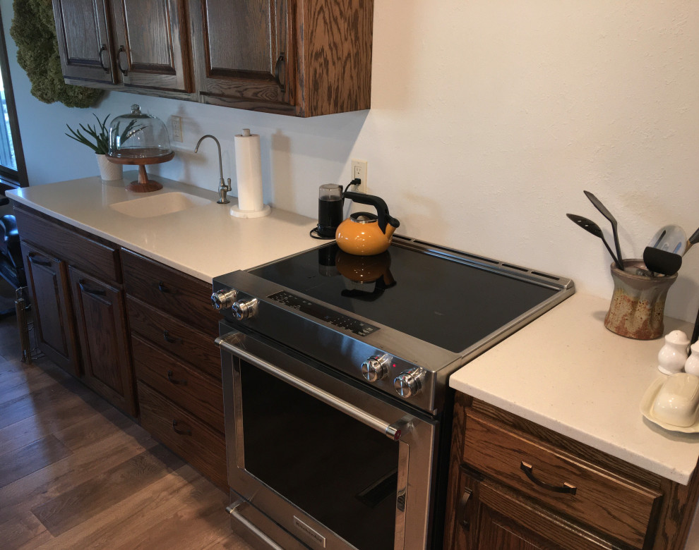 Mid-sized country l-shaped eat-in kitchen in Omaha with a single-bowl sink, raised-panel cabinets, dark wood cabinets, with island and white benchtop.