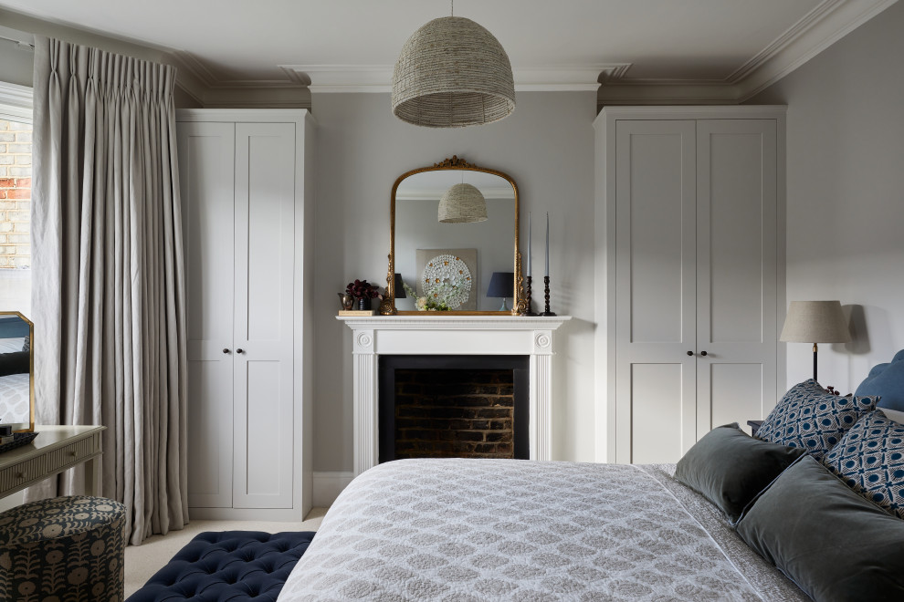 ロンドンにあるトラディショナルスタイルのおしゃれな主寝室 (グレーの壁、カーペット敷き、木材の暖炉まわり、ベージュの床) のインテリア