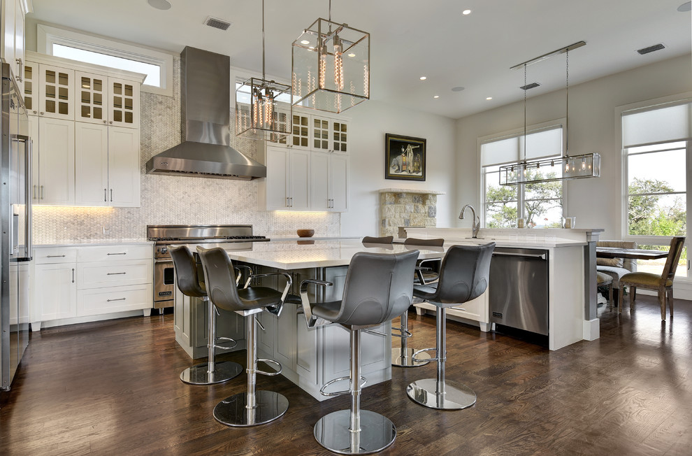 Photo of a large transitional u-shaped eat-in kitchen in Austin with shaker cabinets, white cabinets, white splashback, mosaic tile splashback, stainless steel appliances, dark hardwood floors, with island, quartz benchtops and a farmhouse sink.
