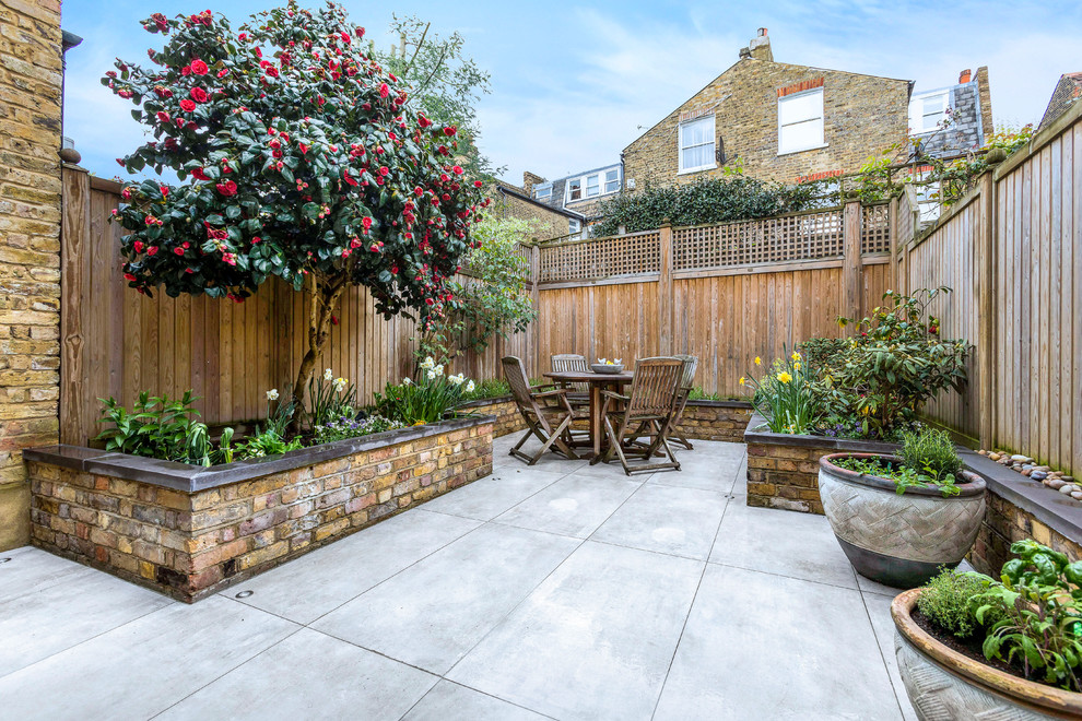 This is an example of a mid-sized traditional backyard patio in London with a container garden, natural stone pavers and no cover.