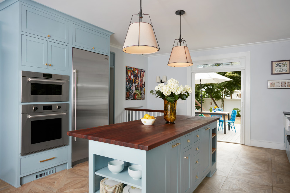 Example of a large transitional porcelain tile and beige floor eat-in kitchen design in New York with a farmhouse sink, beaded inset cabinets, blue cabinets, wood countertops, multicolored backsplash, ceramic backsplash, stainless steel appliances, an island and brown countertops