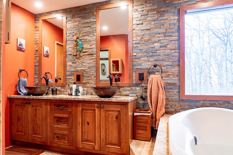 This is an example of a large master bathroom in Columbus with raised-panel cabinets, medium wood cabinets, a drop-in tub, an alcove shower, a one-piece toilet, gray tile, slate, orange walls, travertine floors, a vessel sink, marble benchtops, beige floor, a hinged shower door, multi-coloured benchtops, an enclosed toilet, a double vanity and a freestanding vanity.