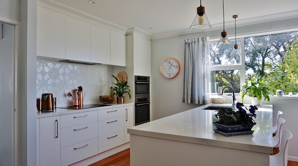 Design ideas for a large single-wall eat-in kitchen in Auckland with a triple-bowl sink, raised-panel cabinets, white cabinets, granite benchtops, white splashback, metal splashback, stainless steel appliances, medium hardwood floors, with island, brown floor and white benchtop.