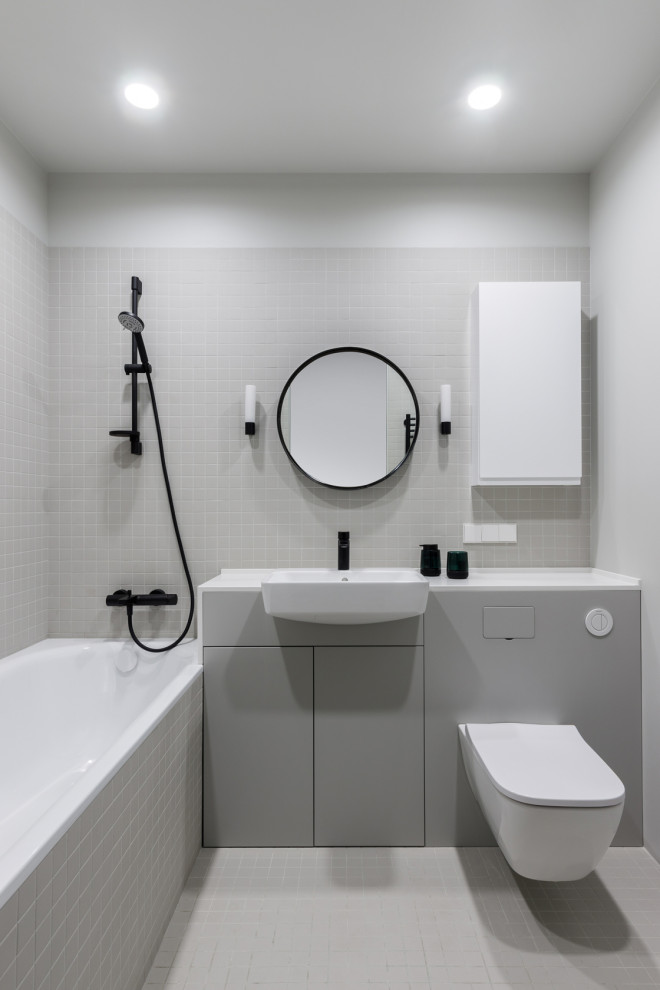 This is an example of a medium sized contemporary grey and white ensuite bathroom in Moscow with flat-panel cabinets, grey cabinets, a submerged bath, a shower/bath combination, a wall mounted toilet, white tiles, porcelain tiles, white walls, porcelain flooring, a built-in sink, engineered stone worktops, white floors, a shower curtain, white worktops, an enclosed toilet, a single sink and a built in vanity unit.