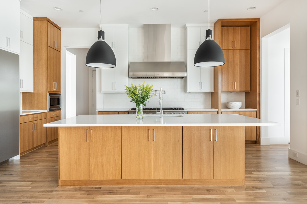 Large contemporary l-shaped open plan kitchen in Dallas with flat-panel cabinets, medium wood cabinets, quartz benchtops, white splashback, ceramic splashback, stainless steel appliances, medium hardwood floors, with island, white benchtop and an undermount sink.