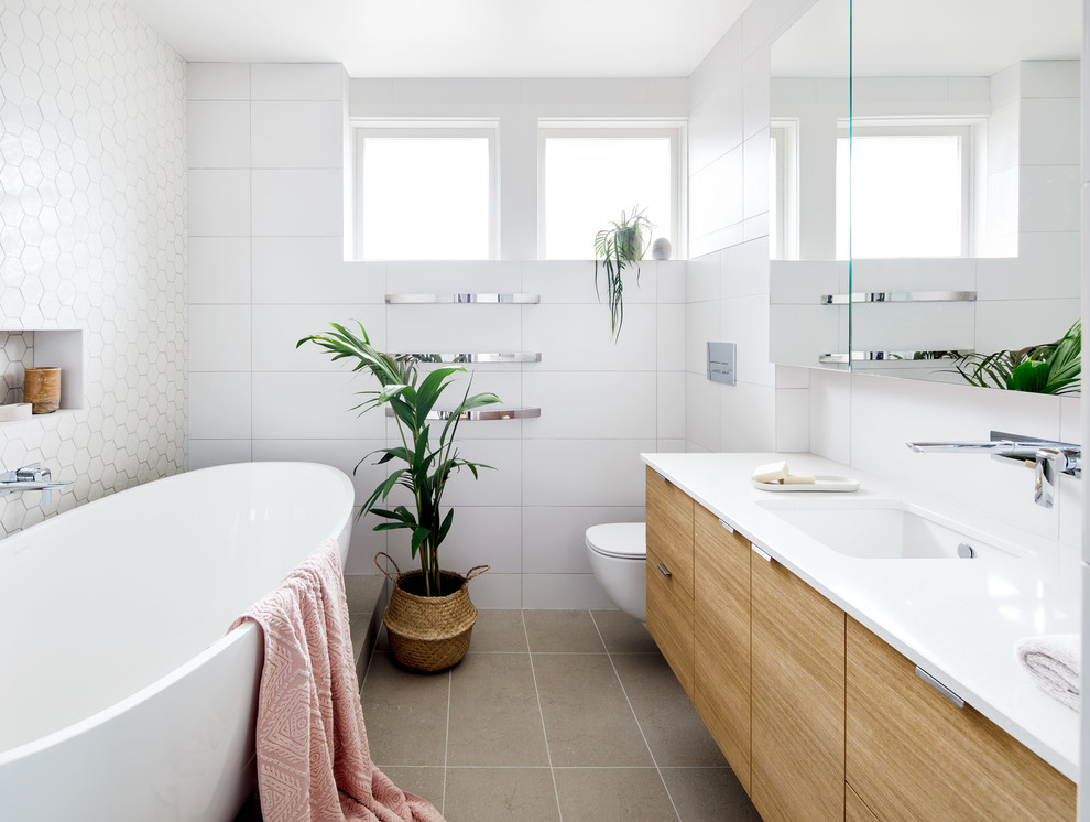 Mid-sized contemporary master bathroom in Melbourne with a freestanding tub, a wall-mount toilet, white tile, ceramic tile, white walls, ceramic floors, an undermount sink, engineered quartz benchtops, white benchtops, flat-panel cabinets, light wood cabinets and beige floor.