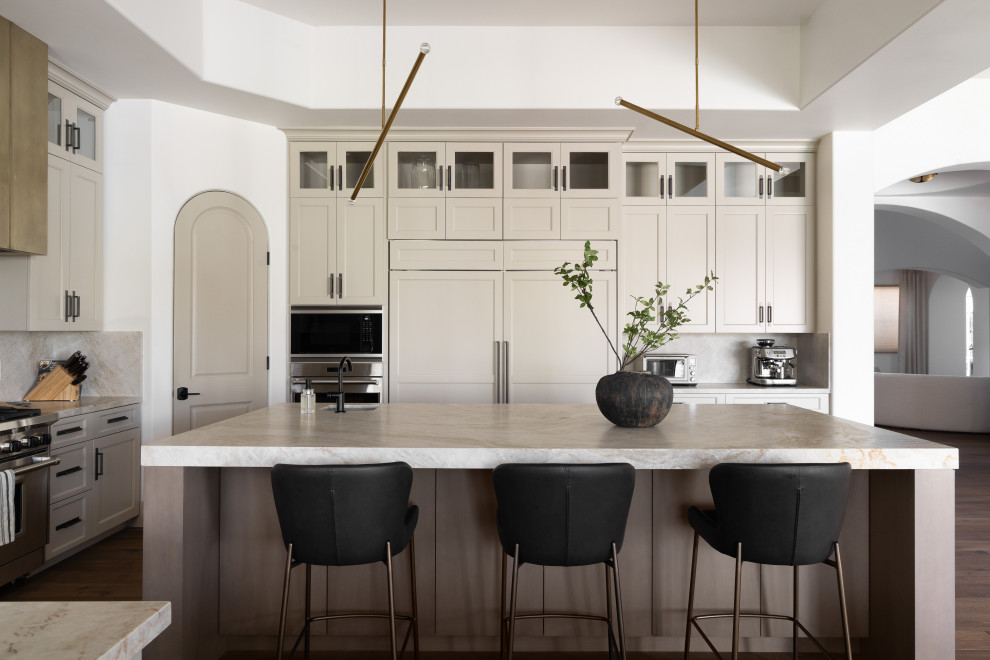 Example of a transitional u-shaped dark wood floor, brown floor and tray ceiling open concept kitchen design in Phoenix with an undermount sink, shaker cabinets, beige cabinets, beige backsplash, stone slab backsplash, stainless steel appliances, an island and beige countertops