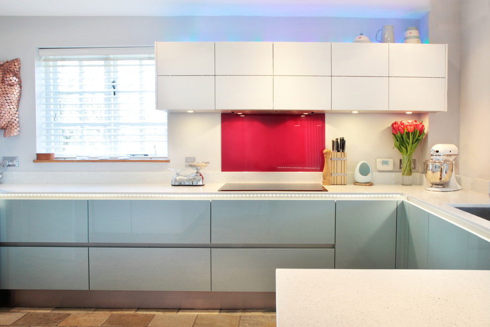 Large contemporary u-shaped open plan kitchen in Buckinghamshire with red splashback, stainless steel appliances, a peninsula, an integrated sink, flat-panel cabinets, blue cabinets, quartzite benchtops, glass sheet splashback and laminate floors.