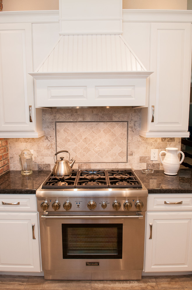 Mid-sized transitional galley porcelain tile and beige floor enclosed kitchen photo with a triple-bowl sink, raised-panel cabinets, white cabinets, granite countertops, beige backsplash, porcelain backsplash, stainless steel appliances and a peninsula