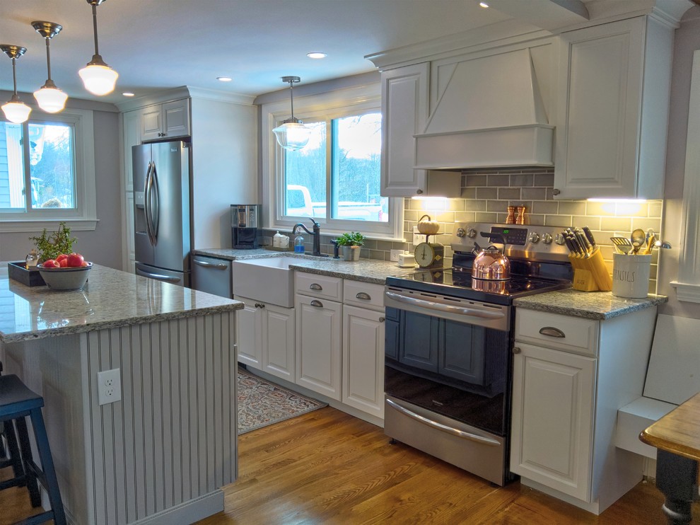 This is an example of a mid-sized country galley kitchen in Boston with a farmhouse sink, raised-panel cabinets, white cabinets, beige splashback, subway tile splashback, stainless steel appliances, light hardwood floors, with island and green benchtop.