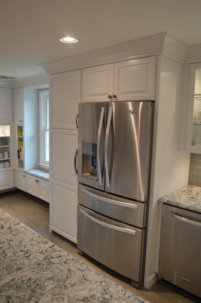 Inspiration for a large transitional u-shaped ceramic tile and gray floor home design remodel with a farmhouse sink, raised-panel cabinets, white cabinets, quartz countertops, gray backsplash, glass tile backsplash, stainless steel appliances and an island