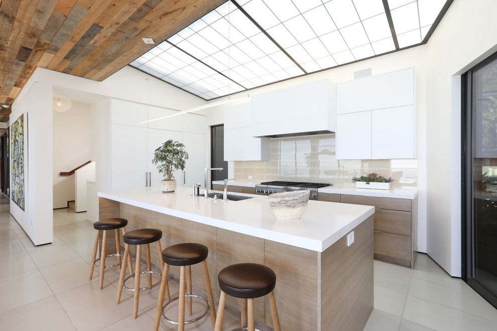 Design ideas for a mid-sized contemporary l-shaped open plan kitchen in Orange County with an undermount sink, flat-panel cabinets, white cabinets, solid surface benchtops, beige splashback, porcelain floors, with island, beige floor and white benchtop.