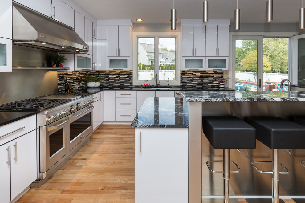 Example of a large trendy u-shaped light wood floor open concept kitchen design with an undermount sink, flat-panel cabinets, white cabinets, granite countertops, multicolored backsplash, mosaic tile backsplash, stainless steel appliances and an island
