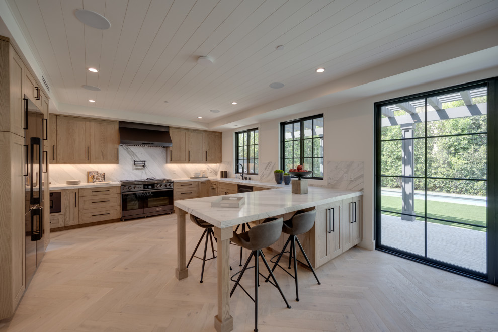 Design ideas for a large country u-shaped eat-in kitchen in Los Angeles with a single-bowl sink, shaker cabinets, grey cabinets, marble benchtops, white splashback, stone slab splashback, black appliances, light hardwood floors, a peninsula, beige floor, white benchtop and timber.