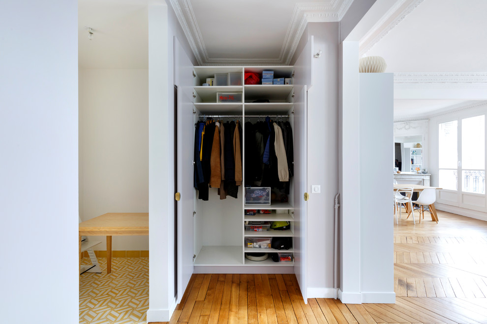 Photo of a small contemporary gender-neutral built-in wardrobe in Paris with white cabinets and medium hardwood floors.