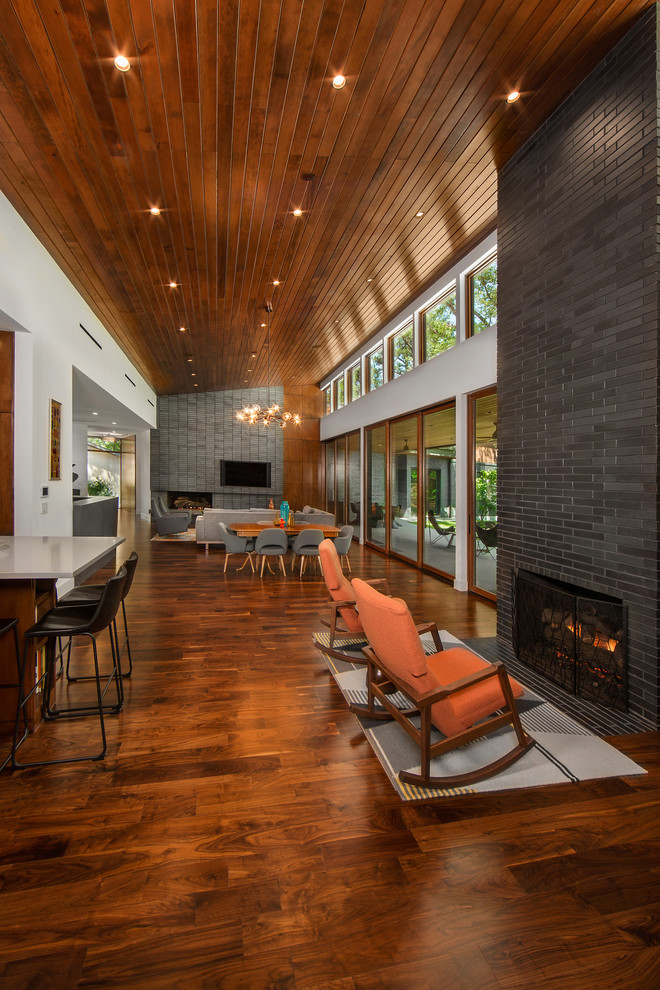 Design ideas for a mid-sized midcentury open concept family room in Dallas with white walls, medium hardwood floors, a standard fireplace, a brick fireplace surround, a wall-mounted tv and brown floor.